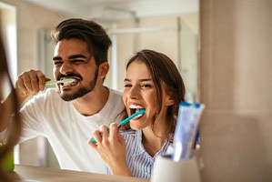 Couple smiling while brushing teeth in bathroom